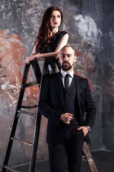 Fameous couple, businessman stay near stepladder and looking at camera. Ginger woman standing on old stepladder. Studio shot