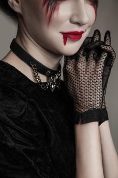 Young beautiful gothic woman with white skin and red lips with bloody drops wearing black collar with spikes. Red smokey eyes. Halloween makeup.