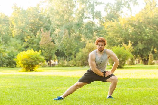 Workout in summer morning. Muscules redhead athlete, doing gymnastic and looking at camera