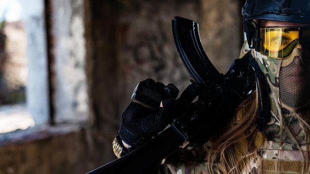 Portrait of a woman in a helmet and goggles with a machine gun in her hands. A female soldier in a camouflage uniform holds a weapon