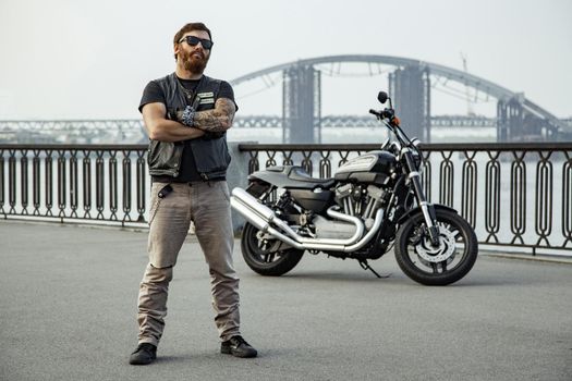 bearded motorcyclist man with his motorbike on summertime posing.