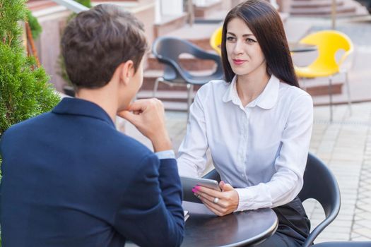 Two friends sitting outdoor in cafe thinking, looking at tablet and discussing their business.