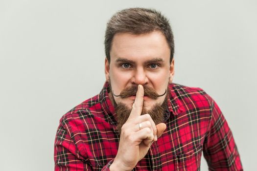Shh sign. Anger businessman with beard and handlebar mustache looking at camera with silent sign. studio shot, on gray background.