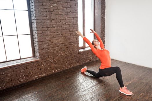 Sexy woman in sportswear squat in front of window and hands up. Studio shot