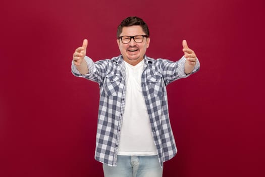 Portrait of happy glad to seeing handsome middle aged business man in casual checkered shirt and eyeglasses standing toothy smile, and want to hugging. studio shot, isolated on dark red background.
