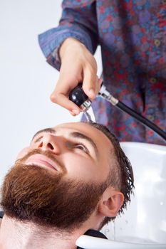 Hairstyling. Cropped image of barber washing head of his client in barber shop while preparing to haircut