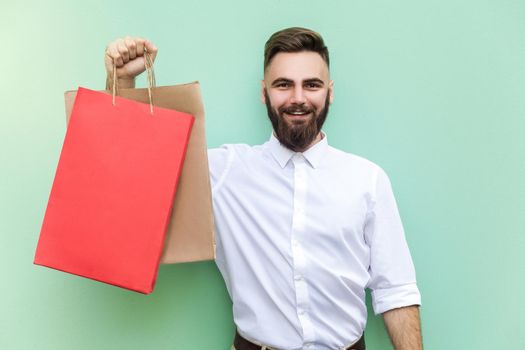 Young adult bearded man holding with many shopping bags at mall or store. Studio shot