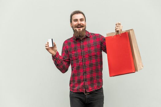 Young adult businessman using credit card for online shopping or banking. Holding card on hands and looking at camera and smile. Indoor, studio shot. Gray background