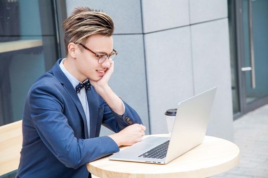 Attractive young freelancer with blue casual suit with laptop and coffee sitting and working. looking at display and smilling.