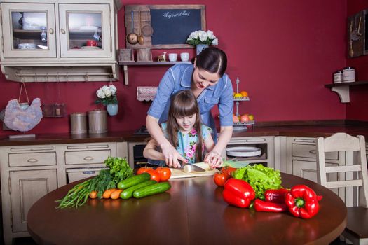 Happy mother and daughter enjoy making and having healthy meal together at their kitchen. they are making vegetable salad and having fun together. mom take care of her daughter and tech how to cook.