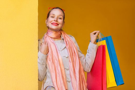 The beautiful bun haired woman in casual clothing with shopping bags, looking at camera with smiling. Sales, shop, retail, consumer concept. Isolated studio shot on yellow background