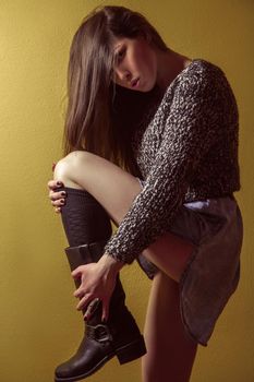 Beautiful young asian model in blue denim skirt and black blouse and fashion makeup posing sitting on stepladder and looking at camera. Studio shot. High-fashion photo.