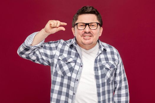I need a few more. Portrait of hopeful handsome middle aged man in checkered shirt, eyeglasses standing, looking at camera and asking for something more. studio shot, isolated on dark red background.