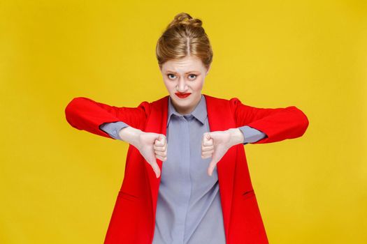 Ginger red head business woman in red suit showing dislike sign. Studio shot, isolated on yellow background