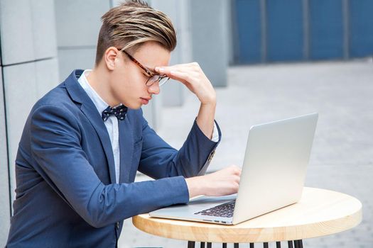 Attractive young freelancer with blue casual suit with laptop and coffee sitting and working. closed eyes and thinking.