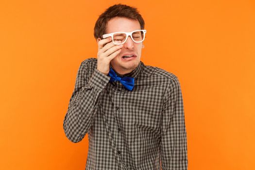 Emotional man crying and wipes away tears. Studio shot. Isolated on orange background