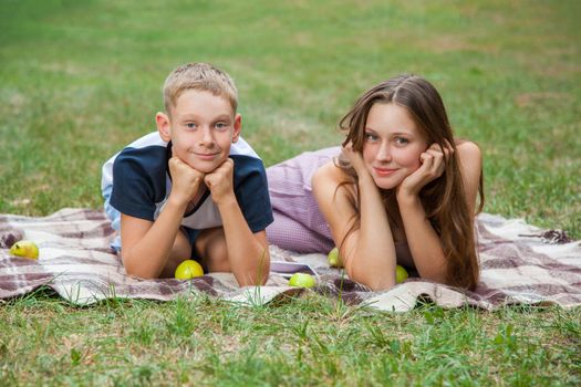 young beautiful brother and sister resting in the garden, looking at camera with smile. picnic summer time. lie down, top view.