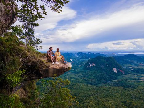 Dragon Crest mountain Krabi Thailand, a Young traveler sits on a rock that overhangs the abyss, with a beautiful landscape. Dragon Crest or Khuan Sai at Khao Ngon Nak Nature Trail in Krabi, Thailand