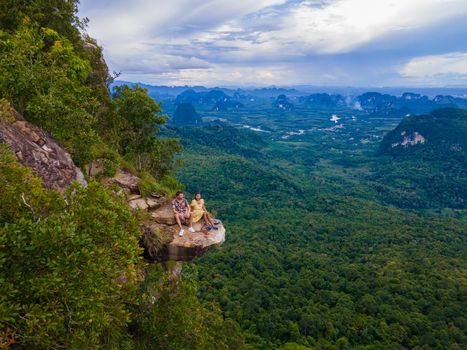 Dragon Crest mountain Krabi Thailand, a Young traveler sits on a rock that overhangs the abyss, with a beautiful landscape. Dragon Crest or Khuan Sai at Khao Ngon Nak Nature Trail in Krabi, Thailand