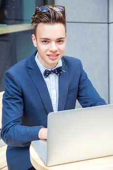 Attractive young freelancer with blue casual suit with laptop and coffee sitting and working. looking at camera and smilling.