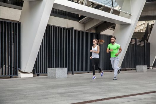 Active happy young couple jogging side by side in an urban street during their daily workout in a health and fitness concept. using sport watch.