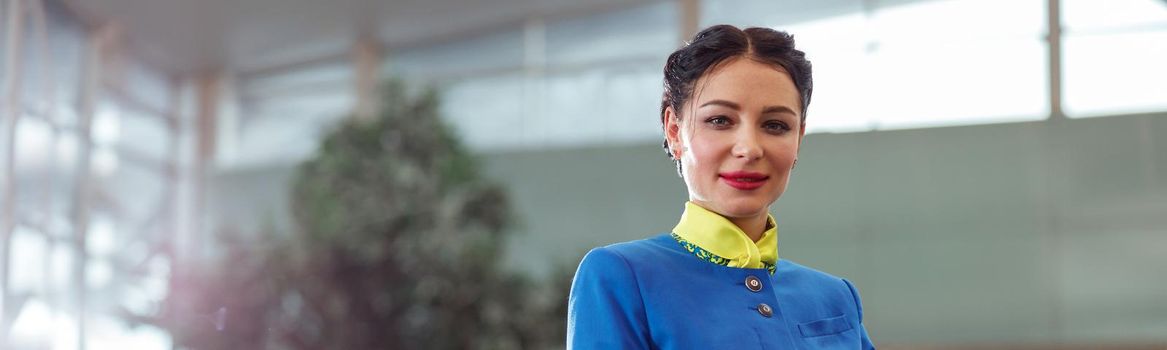 Female air hostess or stewardess wearing blue aviation uniform and gloves while looking at camera and smiling