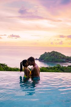 a young couple of men and women at a swimming pool during a vacation on a tropical island. man and woman in infinity pool during sunset. luxury vacation in Thailand pool of a luxury pool villa