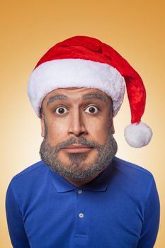 The colored caricature of the funny santa clause with big head and blue shirt, red hat with gray beard, surprised looking at camera on orange background..young man with old senior bearded face retouch