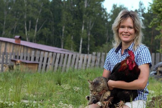 Beautiful woman in the chicken farm holding a chicken, healthy lifestyle and organic farming concept. Rooster and cat