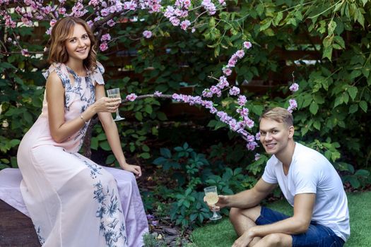 Young adult man says a toast. Holding Champagne glass, toothy smiling. Outdoor shot, spring park or summer concept. Love, sensual people