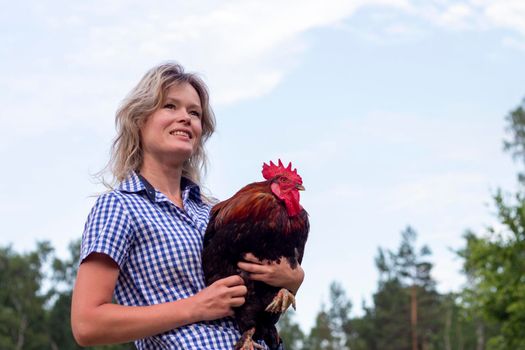Beautiful woman in the chicken farm holding a chicken, healthy lifestyle and organic farming concept. Rooster and cat