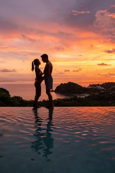 a young couple of men and women at a swimming pool during a vacation on a tropical island. man and woman in infinity pool during sunset. luxury vacation in Thailand pool of a luxury pool villa