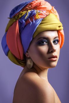 Beautiful woman with colored headwear and blue makeup, studio shot on purple background