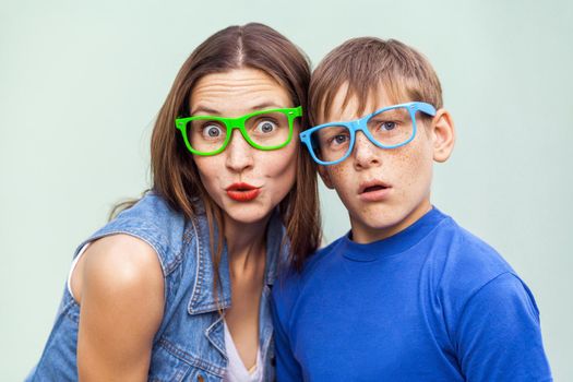 Family, emotions and feelings. Older sister and her brother with freckles, posing over light blue background together on summer time, looking at camera with surprised face. Indoor studio shot