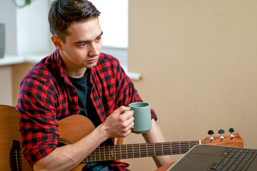 Young man working on laptop sitting near coffee table with cup of hot drink tea and enjoing sunset view. Slow living