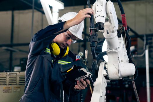 Young factory worker working with adept robotic arm in a workshop . Industry robot programming software for automated manufacturing technology .