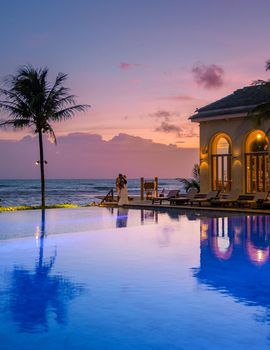 a young couple of men and women at a swimming pool during a vacation on a tropical island. man and woman in infinity pool during sunset. luxury vacation in Thailand pool of a luxury pool villa