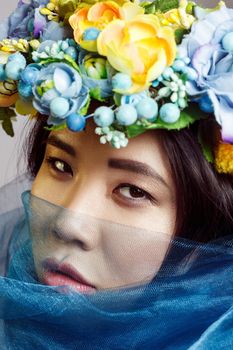 portrait of asian woman with floral hat and blue veil looking at camera on light grey background . indoor studio shot.