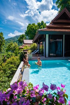 a young couple of men and women at a swimming pool during a vacation on a tropical island. man and woman in infinity pool during sunset. luxury vacation in Thailand pool of a luxury pool villa