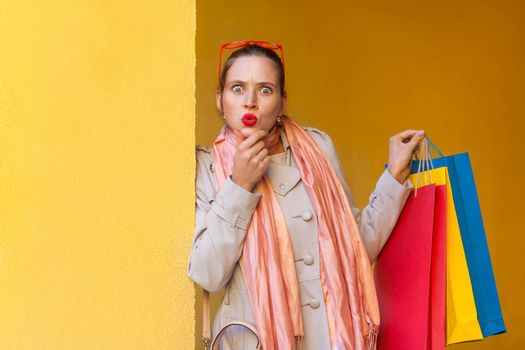 Three beautiful woman after shopping. Looking at camera with shocked face, and wonder, because thay got gift from shop. Isolated on yellow background. Studio shot