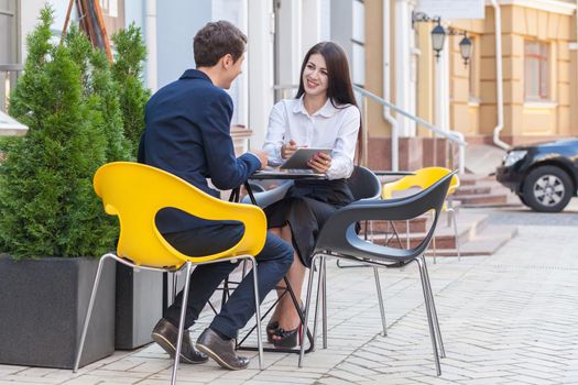 Two friends sitting outdoor in cafe thinking, looking at tablet and discussing their business.