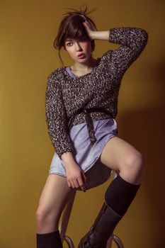 Beautiful young asian model in blue denim skirt and black blouse and fashion makeup posing sitting on stepladder and looking at camera. Studio shot. High-fashion photo.