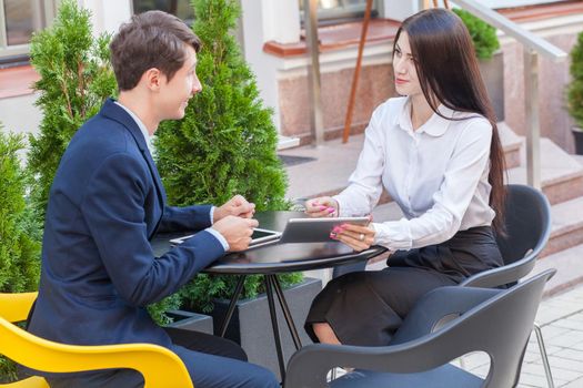 Two friends sitting outdoor in cafe thinking, looking at tablet and discussing their business.