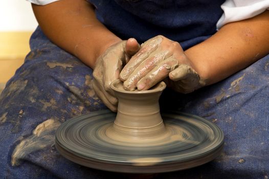 Potter modeling ceramic pot from clay on a potter's wheel.