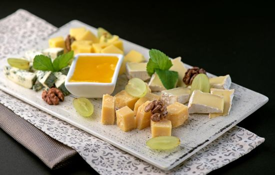Cheese platter with a variety of types of cheese - gorgonzola, mozzarella, , camembert, toma, emmental and fresh caprino on black background