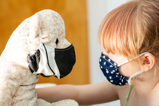 Young girl training to use a face mask during the pandemic -Focus on the teddy.