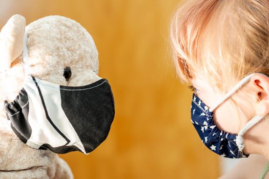 Young girl training to use a face mask during the pandemic -Focus on the teddy.