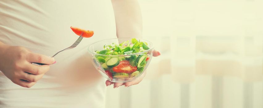 A pregnant woman eats a salad with vegetables. Selective focus. Food.