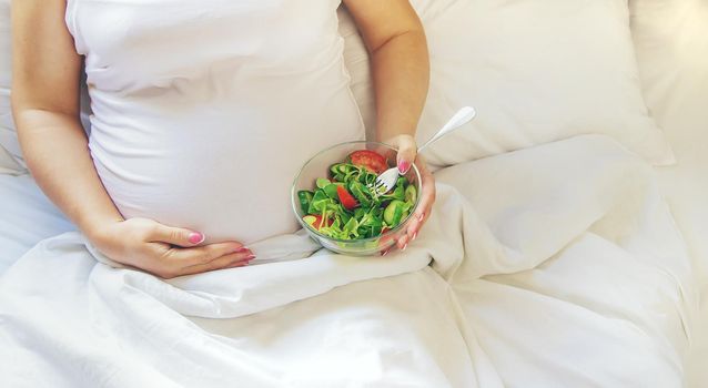 A pregnant woman eats a salad with vegetables. Selective focus. Food.