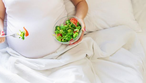 A pregnant woman eats a salad with vegetables. Selective focus. Food.